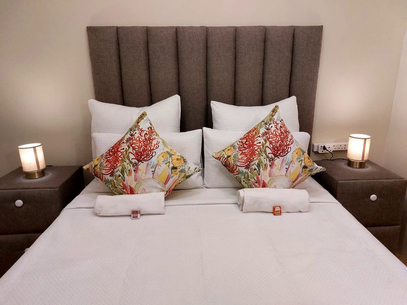 A well-presented bedroom featuring a neutral color palette with a tall upholstered headboard and integrated electrical power points.