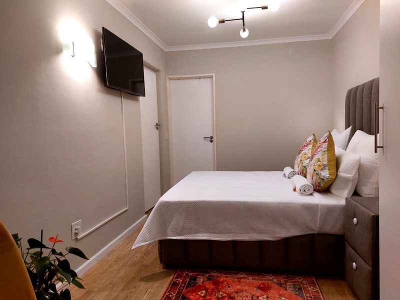 A well-maintained bedroom featuring laminate flooring, modern lighting, and a built-in upholstered headboard, creating a clean and comfortable sleeping space.