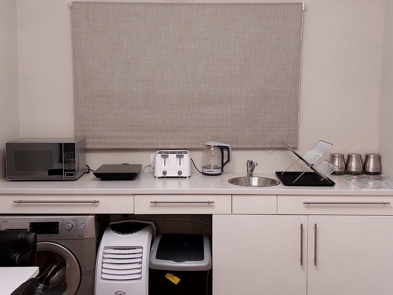 A compact scullery or utility area featuring built-in white cabinetry, a stainless steel sink, and integrated laundry plumbing connections.