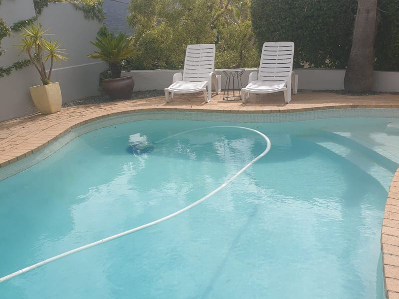 A private swimming pool area featuring brick coping, a surrounding boundary wall, and established garden landscaping.