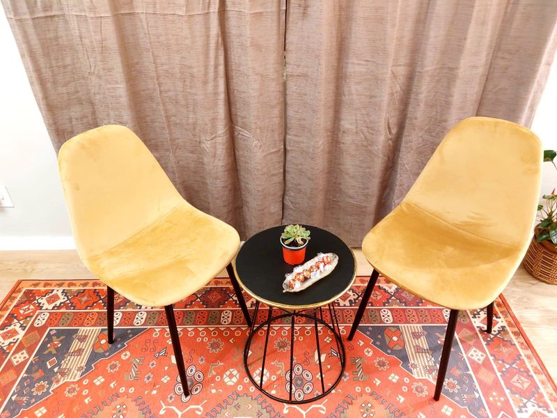 A small seating area featuring a round side table and two yellow velvet chairs set against floor-length curtains.