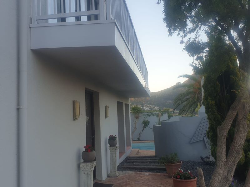 Rear exterior view of the cottage featuring a paved patio area, an elevated balcony, and a swimming pool in the background.