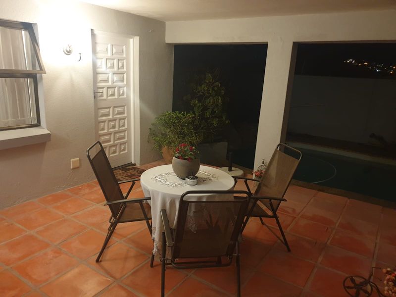 A covered patio area featuring terracotta floor tiles, an exterior door, and a casement window, overlooking the pool area.