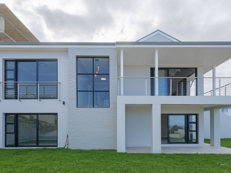 Modern rear elevation featuring a covered patio, upper balcony with stainless steel balustrades, large sliding glass doors, and a well-maintained lawn.