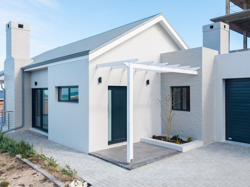 Modern single-story home exterior featuring a clean white facade, brick chimneys, a pergola-covered entrance, and a paved driveway with an integrated garage.