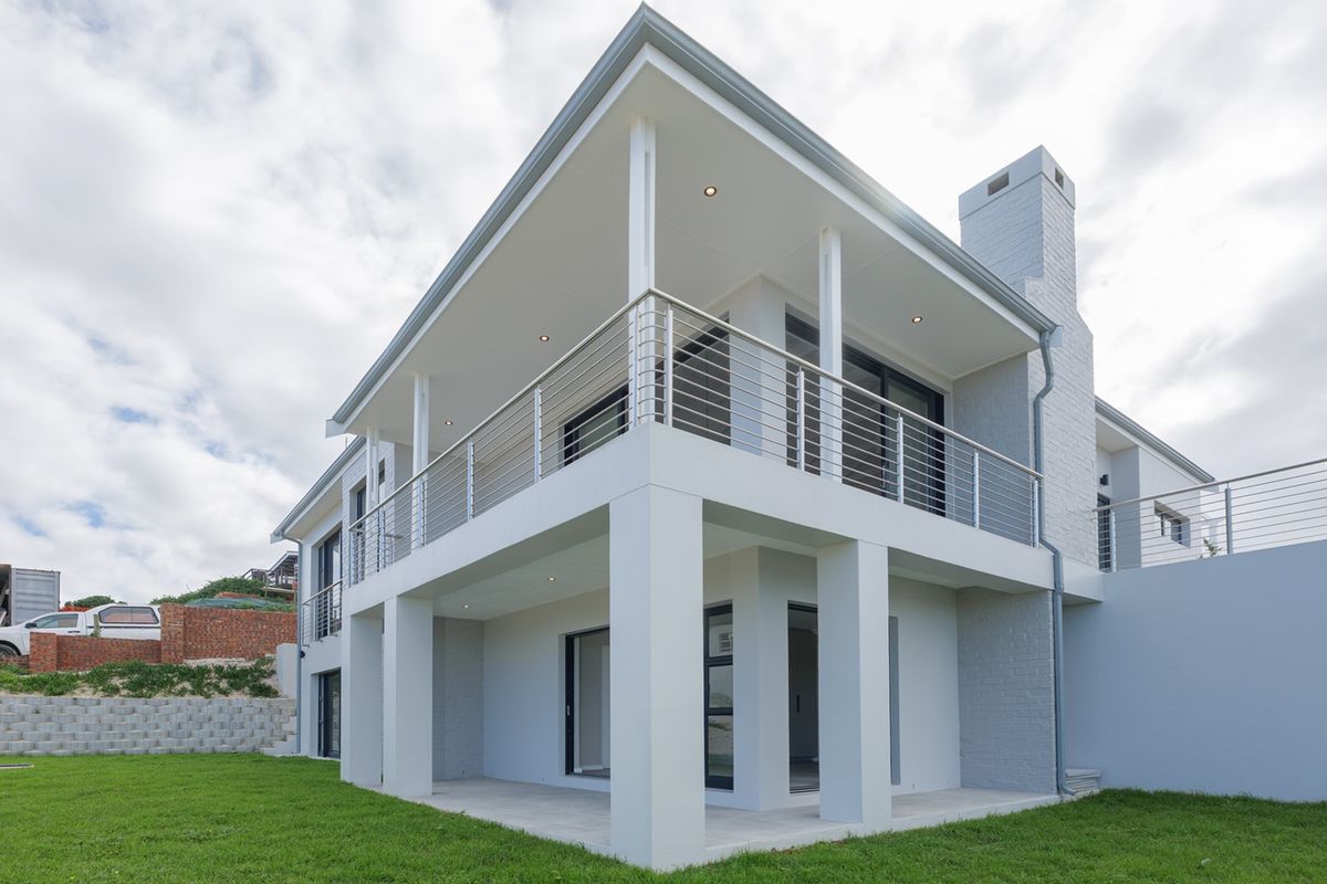 A modern two-story house exterior featuring a spacious covered patio, upper-level balcony with stainless steel railings, and a prominent brick chimney.
