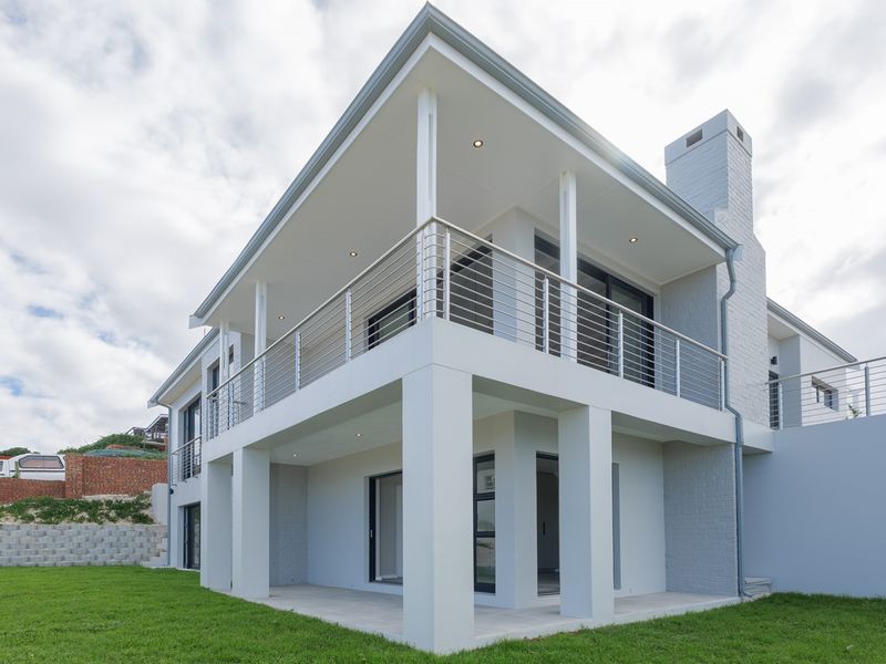 A modern two-story house exterior featuring a spacious covered patio, upper-level balcony with stainless steel railings, and a prominent brick chimney.