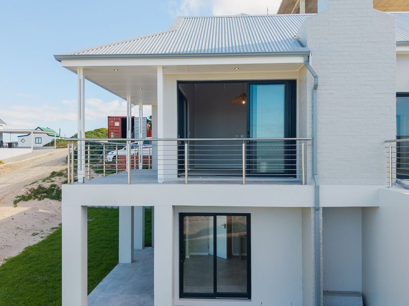 A modern rear elevation featuring a spacious tiled balcony with stainless steel balustrades, sliding glass doors, and a clean, contemporary painted brick finish.