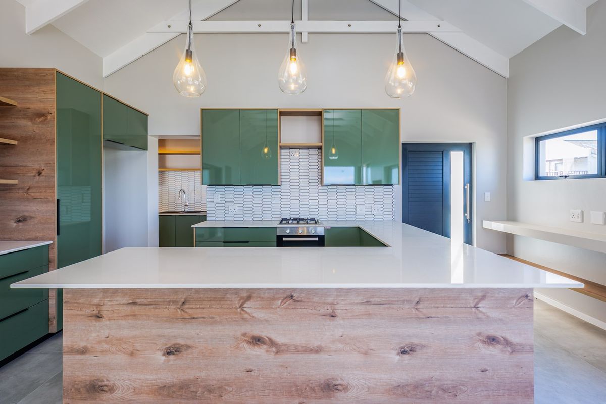 Modern kitchen featuring green cabinetry, wood-grain accents, stone countertops, a gas hob, and a vaulted ceiling with pendant lighting.