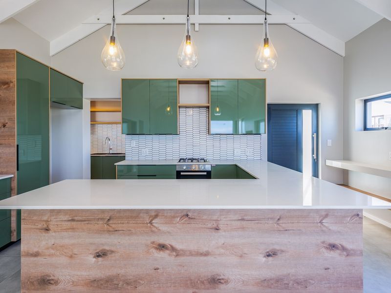 Modern kitchen featuring green cabinetry, wood-grain accents, stone countertops, a gas hob, and a vaulted ceiling with pendant lighting.