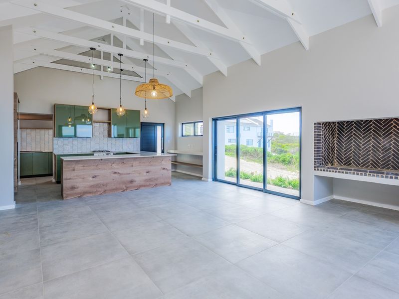 Spacious open-plan living area featuring a vaulted ceiling with exposed trusses, a modern kitchen with island, and a built-in fireplace with herringbone brickwork.