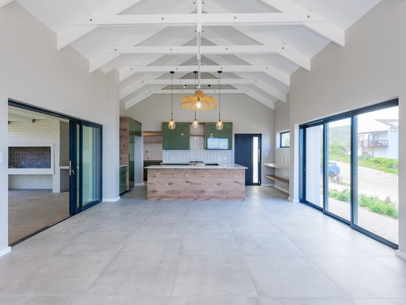 Spacious open-plan living area featuring a modern kitchen with island, vaulted ceilings with exposed trusses, and large sliding doors opening to the exterior.