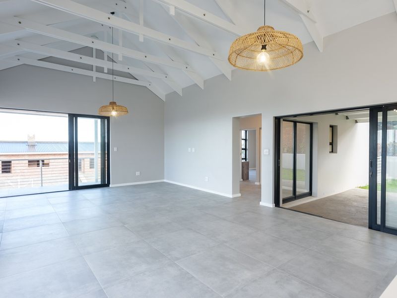Spacious open-plan living area featuring vaulted ceilings with exposed trusses, large sliding doors for natural light, and modern tiled flooring.