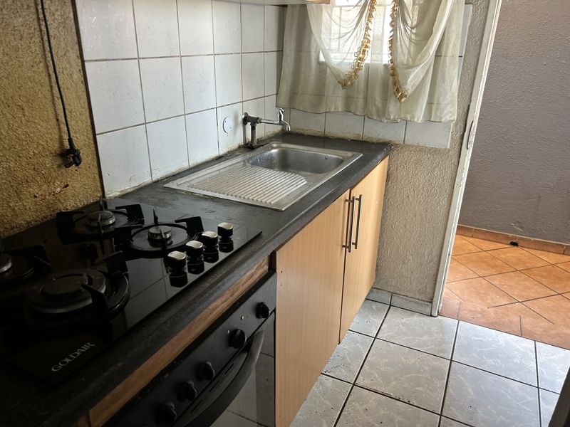 Compact kitchen featuring a built-in oven, gas hob, stainless steel sink, and tiled backsplash with laminate cabinetry.