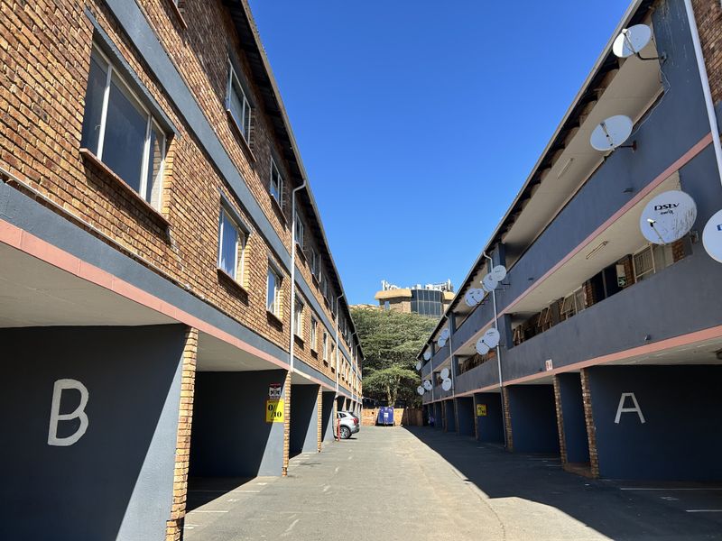 Exterior view of an apartment complex featuring brick facades, covered parking bays, and multiple satellite dishes mounted on the building structure.