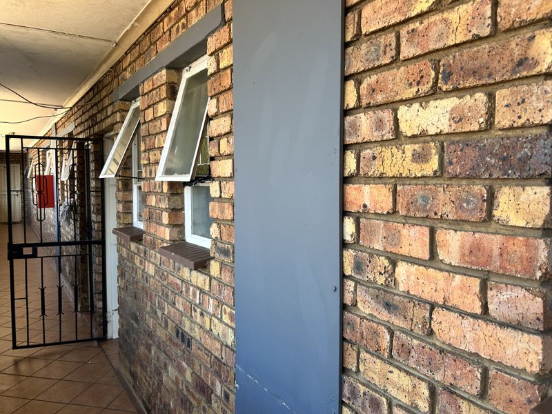 Exterior apartment hallway featuring exposed brick walls, security gate, and top-hung windows.
