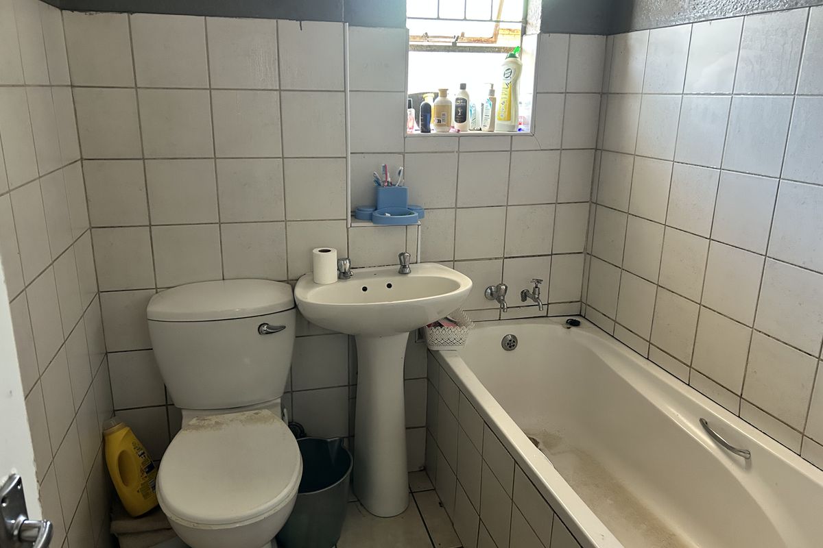 A functional bathroom featuring a pedestal basin, bathtub, and toilet with tiled walls and flooring, requiring cosmetic updates to improve its overall condition.