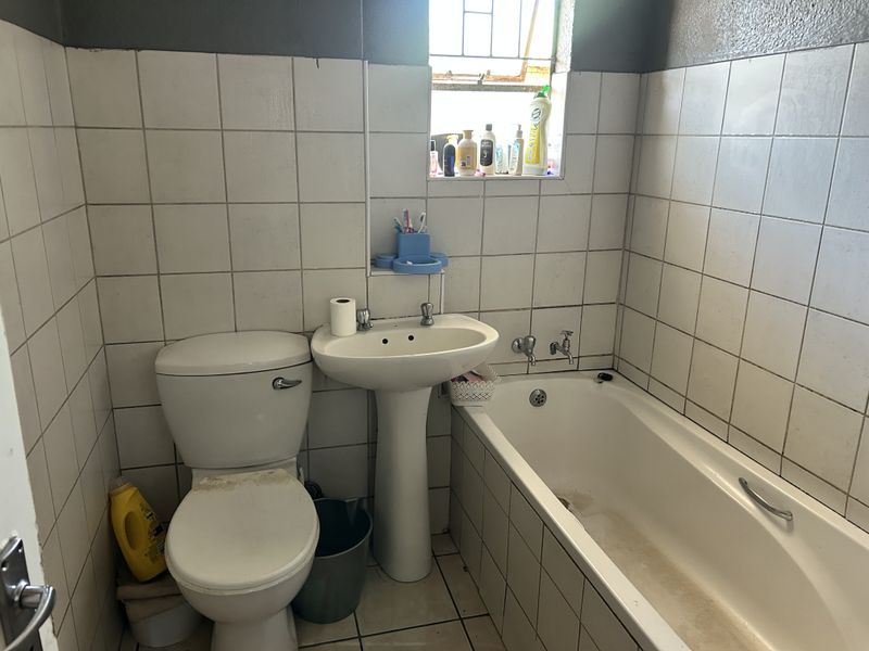 A functional bathroom featuring a pedestal basin, bathtub, and toilet with tiled walls and flooring, requiring cosmetic updates to improve its overall condition.