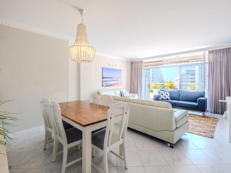 Bright and spacious open-plan living and dining area featuring tiled floors, crown molding, and large sliding glass doors leading to an outdoor balcony.