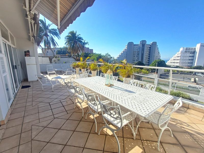 Spacious outdoor balcony featuring tiled flooring, a retractable awning for shade, and a metal balustrade, offering an ideal space for outdoor dining and relaxation.