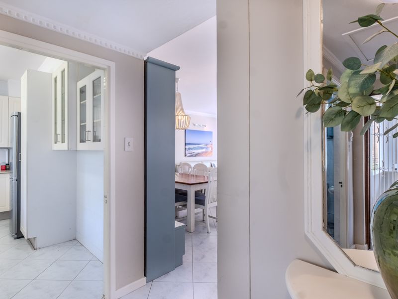 A bright hallway featuring crown molding and tiled flooring, providing a clear view into the adjacent kitchen and dining area.
