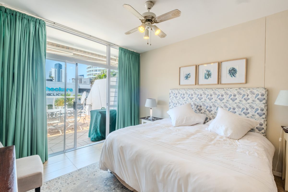 A bright bedroom featuring tiled flooring, a ceiling fan, and large sliding glass doors that open onto a private balcony.