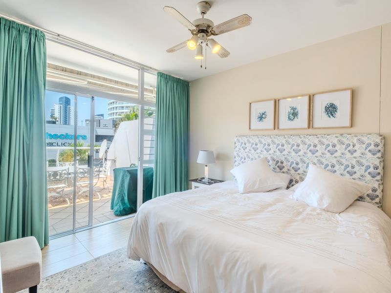 A bright bedroom featuring tiled flooring, a ceiling fan, and large sliding glass doors that open onto a private balcony.