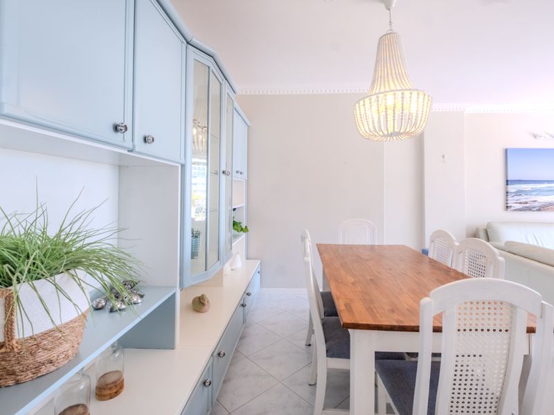 A bright dining area featuring elegant built-in cabinetry, classic crown molding, and stylish pendant lighting, set against neutral walls and tiled flooring.