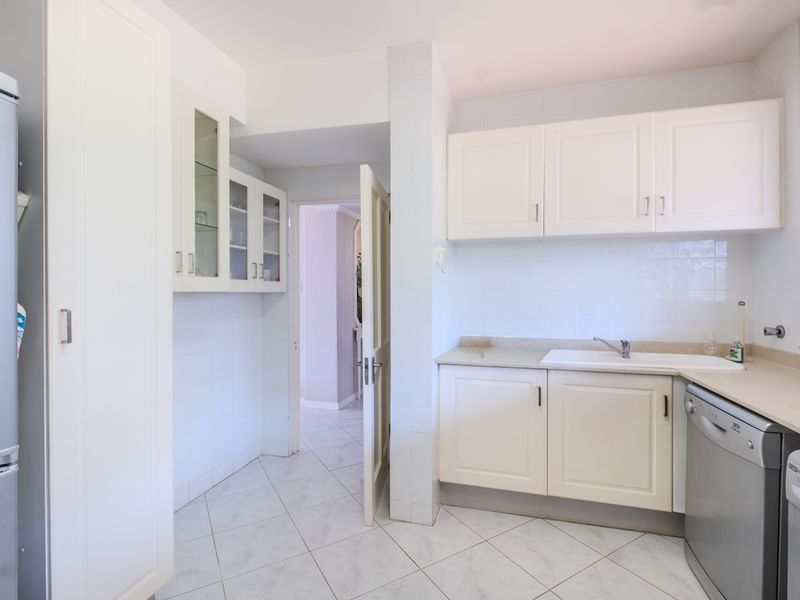 A functional kitchen featuring white cabinetry, tiled backsplash, stone countertops, and tiled flooring, providing a clean and practical workspace.