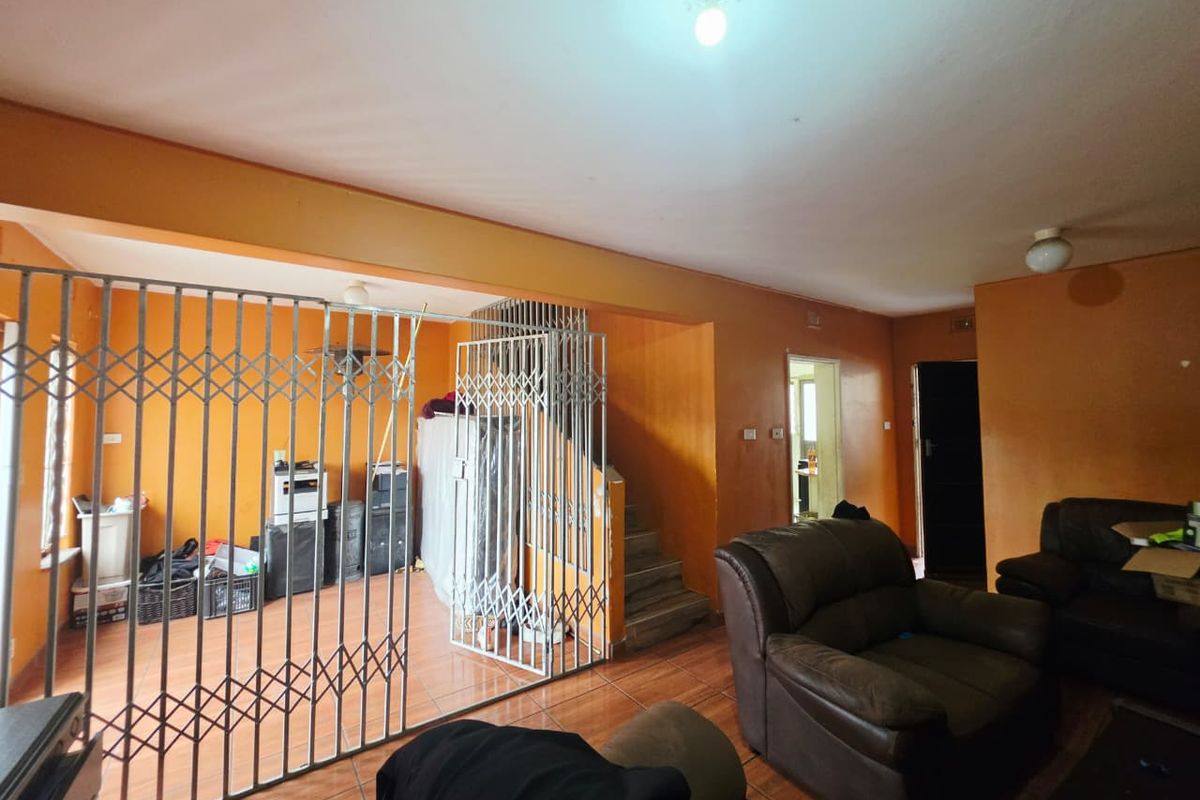Living area featuring tiled flooring, a built-in staircase, and a security gate partition, requiring cosmetic updates to the wall finishes.