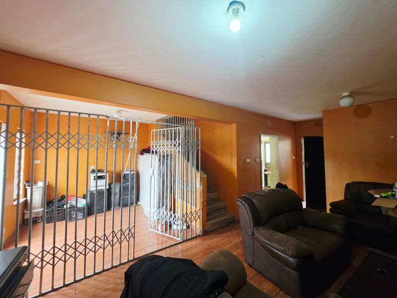 Living area featuring tiled flooring, a built-in staircase, and a security gate partition, requiring cosmetic updates to the wall finishes.