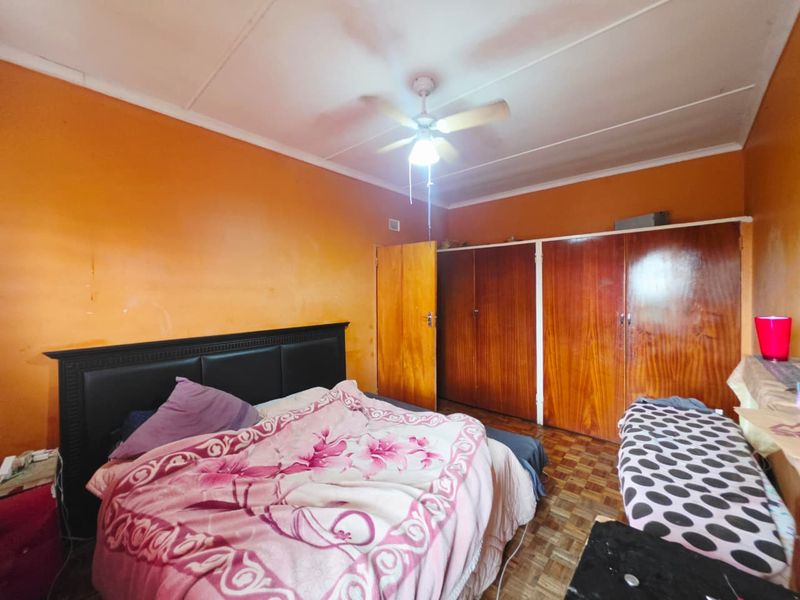 Bedroom featuring built-in wooden cupboards, a ceiling fan, and parquet flooring. The room requires cosmetic updates to the wall finishes.