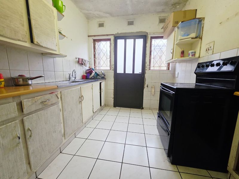 A dated kitchen featuring original cabinetry, tiled flooring, and a freestanding stove, requiring significant renovation and cosmetic updates to modernize the space.