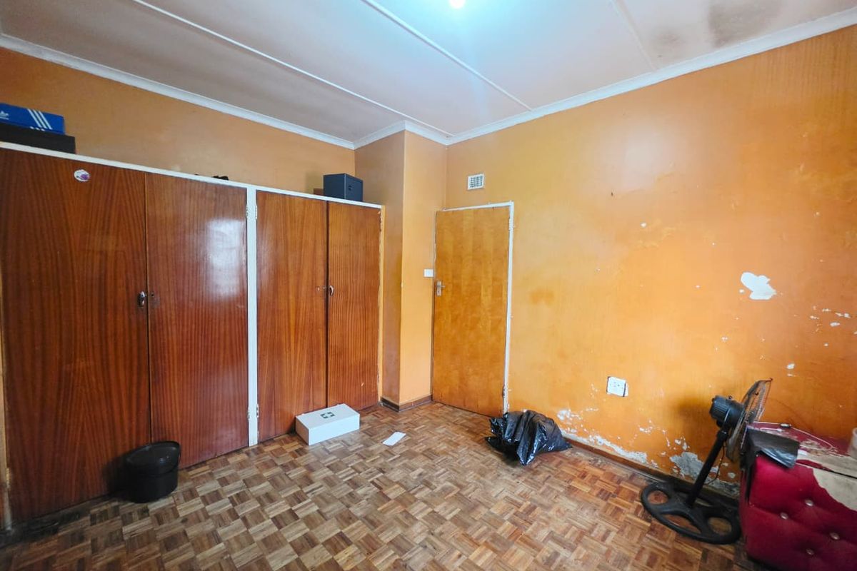 A bedroom featuring parquet flooring and built-in wooden cupboards, requiring cosmetic updates to the walls and ceiling to improve its overall condition.