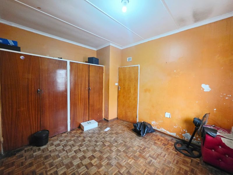 A bedroom featuring parquet flooring and built-in wooden cupboards, requiring cosmetic updates to the walls and ceiling to improve its overall condition.