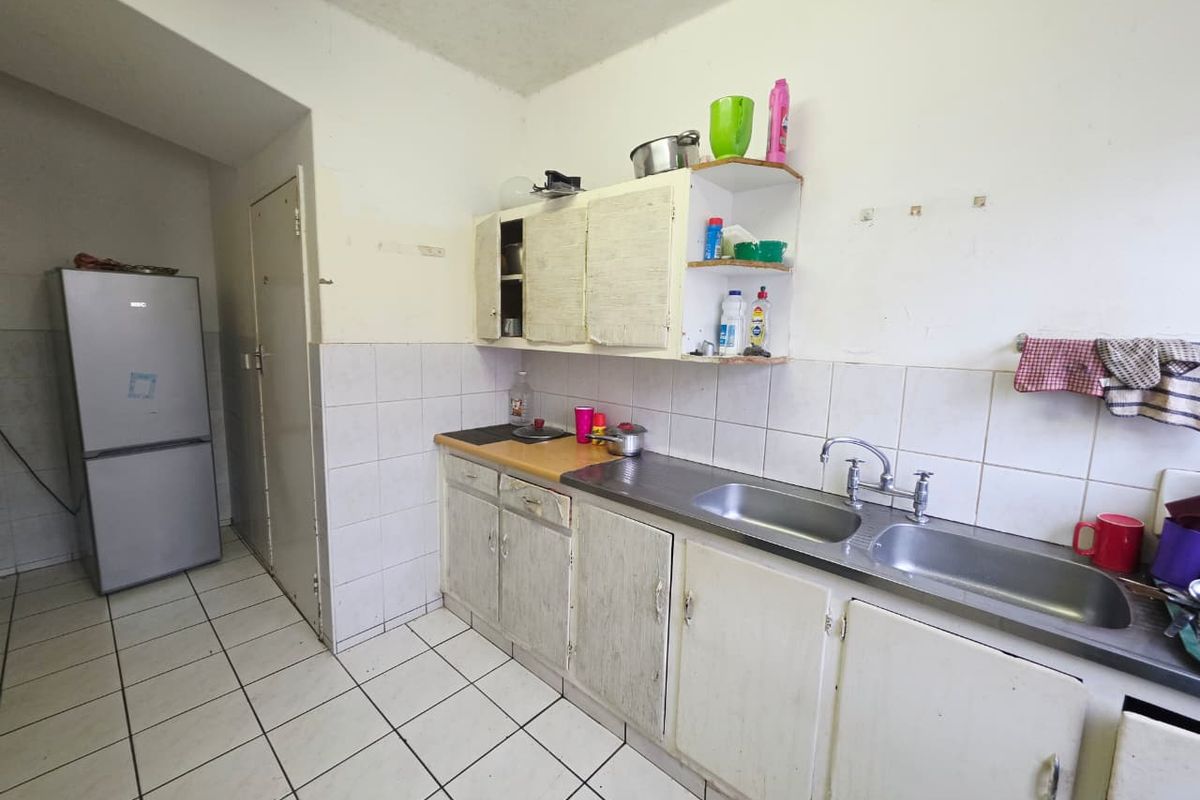 A dated kitchen featuring a double basin stainless steel sink, tiled splashback, and original built-in cabinetry in need of refurbishment.