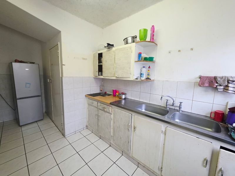 A dated kitchen featuring a double basin stainless steel sink, tiled splashback, and original built-in cabinetry in need of refurbishment.