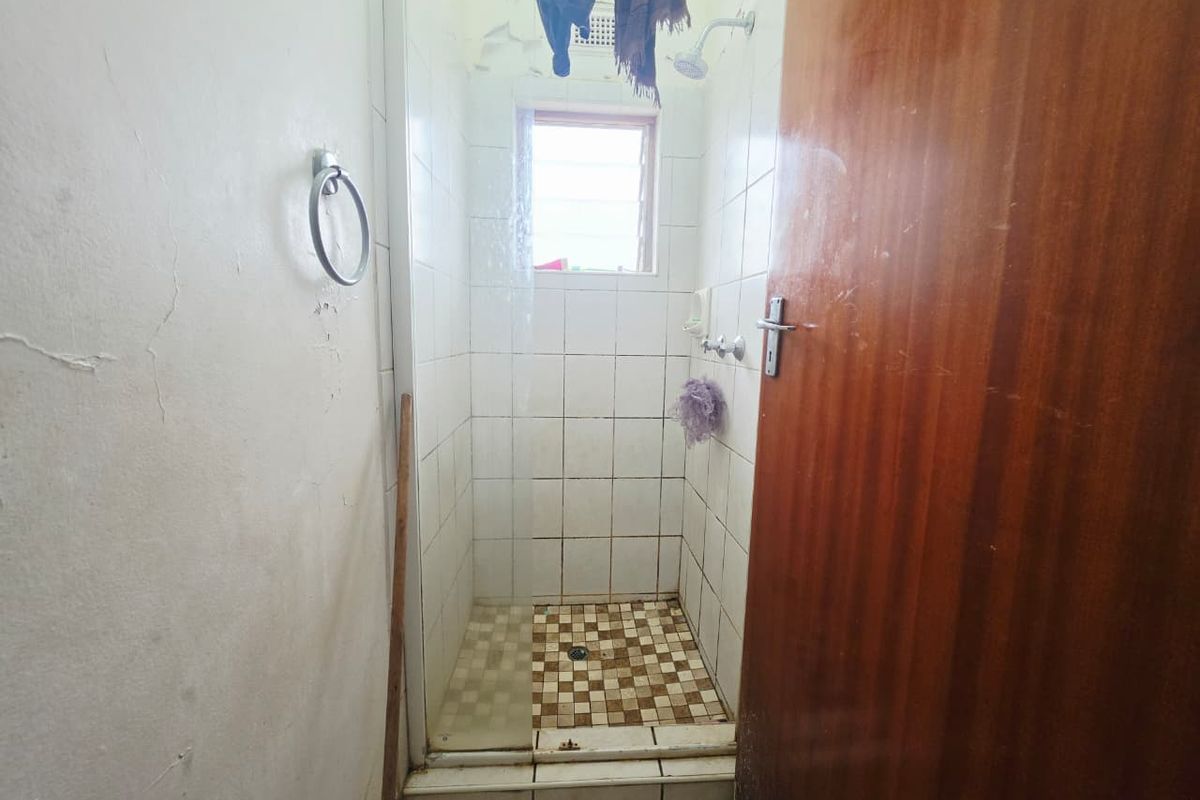 A compact shower stall featuring tiled finishes and a louver window, currently requiring maintenance and cosmetic updates to the ceiling and wall surfaces.