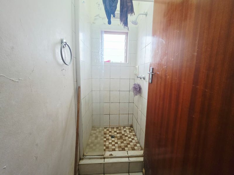 A compact shower stall featuring tiled finishes and a louver window, currently requiring maintenance and cosmetic updates to the ceiling and wall surfaces.
