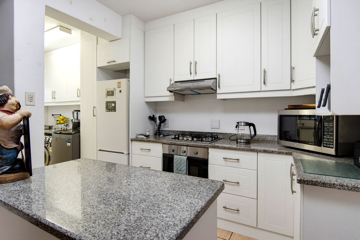 Modern kitchen featuring granite countertops, built-in cabinetry, gas hob, and an integrated oven, with an adjacent scullery area for added convenience.
