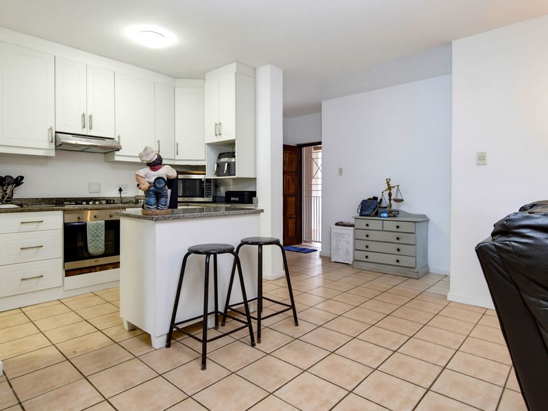 Open-plan kitchen featuring white cabinetry, granite countertops, and built-in appliances, seamlessly flowing into the living area with tiled flooring throughout.