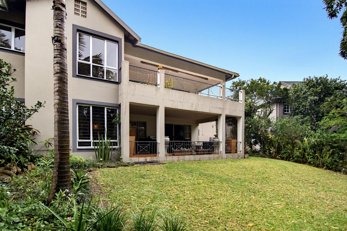 Rear view of the apartment building featuring a covered ground-floor patio, an upper-level balcony with metal railings, and a well-maintained private garden.