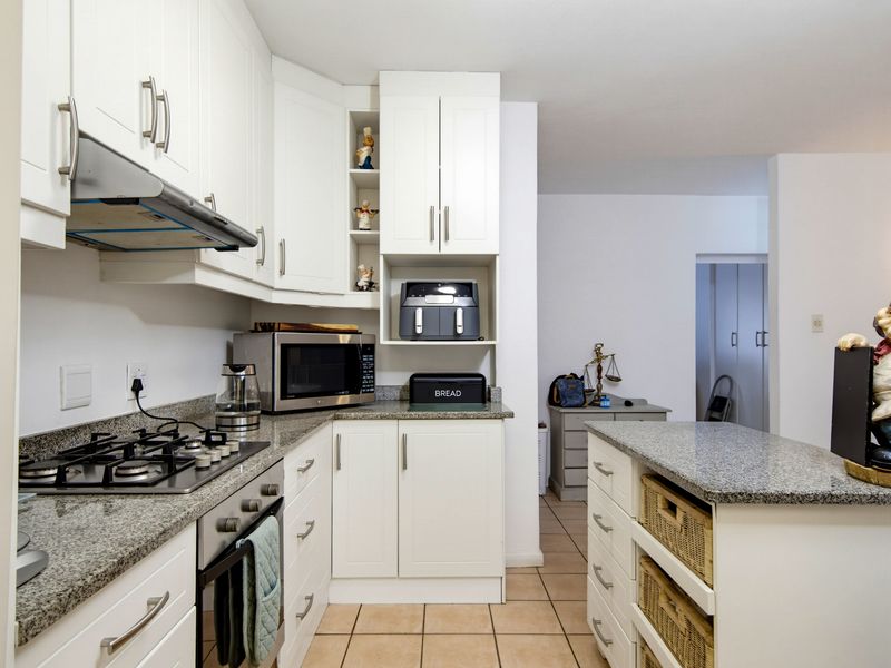 A functional kitchen featuring white cabinetry, granite countertops, a gas hob, and a built-in oven, with tiled flooring throughout.