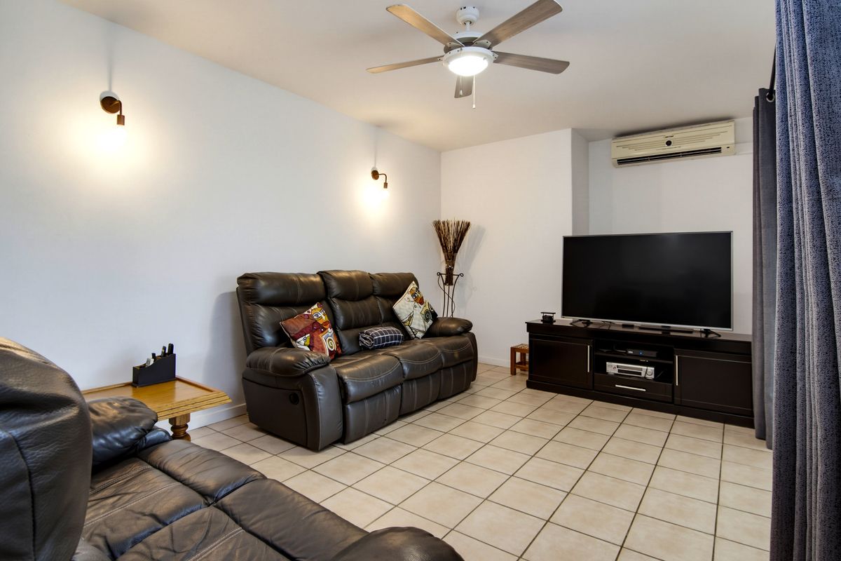 A comfortable living room featuring ceramic tile flooring, a ceiling fan, wall-mounted lighting, and a wall-mounted split-system air conditioning unit.