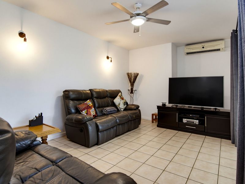 A comfortable living room featuring ceramic tile flooring, a ceiling fan, wall-mounted lighting, and a wall-mounted split-system air conditioning unit.