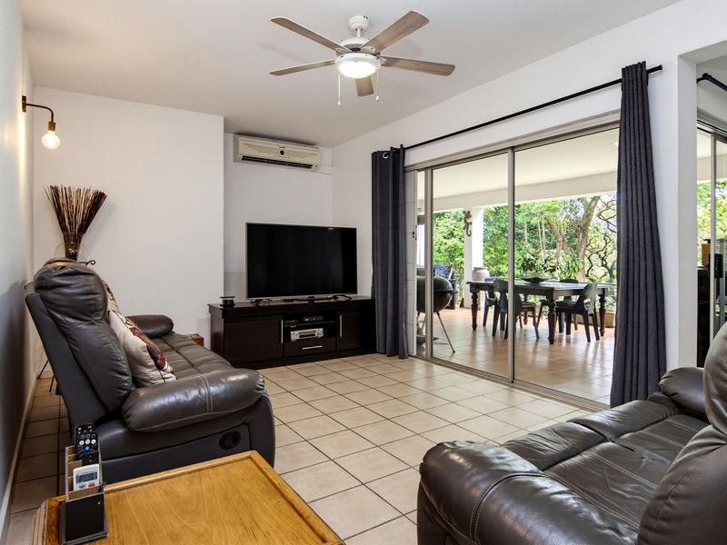 A comfortable living room featuring tiled flooring, a ceiling fan, and large sliding glass doors that provide seamless access to the outdoor patio area.