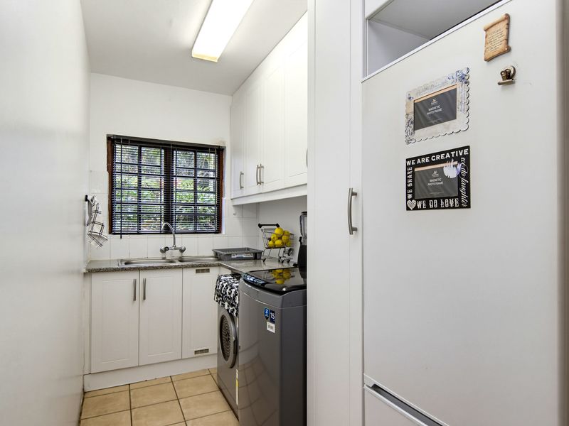 A functional laundry room featuring white built-in cabinetry, a stainless steel sink, and tiled flooring with space for laundry appliances.