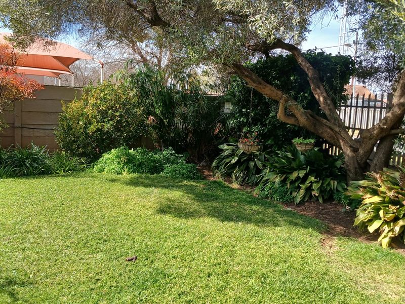 A well-maintained private garden featuring a lush green lawn, mature trees, and established perimeter landscaping with boundary walling.