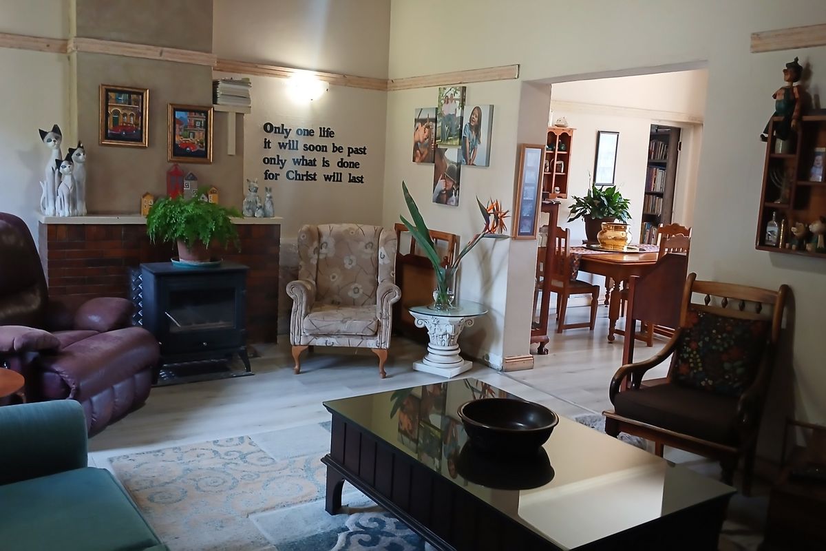 A cozy living room featuring a brick-surround freestanding fireplace, light-toned laminate flooring, and an open-plan flow into the adjacent dining area.