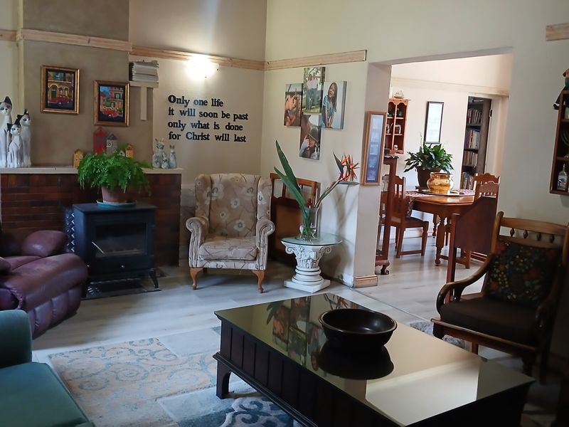 A cozy living room featuring a brick-surround freestanding fireplace, light-toned laminate flooring, and an open-plan flow into the adjacent dining area.